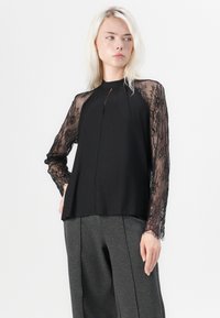 Black blouse with a keyhole opening at the neck, featuring long lace sleeves. The body is smooth fabric, and the fit is relaxed and flowing.
