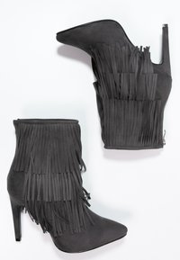 Bottes ankle en suede noir avec des franges, bout pointu et talon aiguille. Fermeture éclair sur le côté. Texture lisse partout.