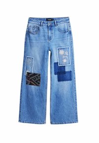 Helle blaue weit geschnittene Jeans mit mehreren Stoffpatches in verschiedenen Mustern und Texturen, darunter florale und geometrische Designs.