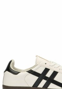 Zapatilla blanca con rayas negras, parte superior de cuero, forro textil, suela de goma, puntera redonda y diseño de cordones. Costuras acentuadas visibles.