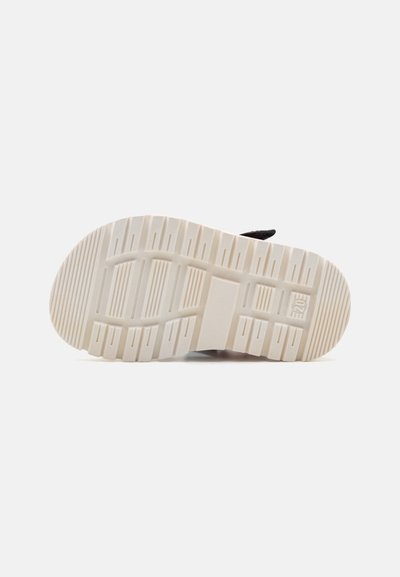 Suela de un zapato con un patrón texturizado y resistente. La suela exterior es de color crema con surcos para mayor tracción y durabilidad.