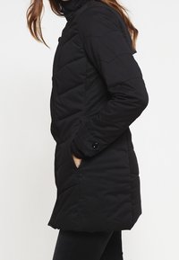 Svart vadderad vinterjacka med hög krage, horisontellt quiltad struktur, framfickor och knapplist. Slim fit-design.