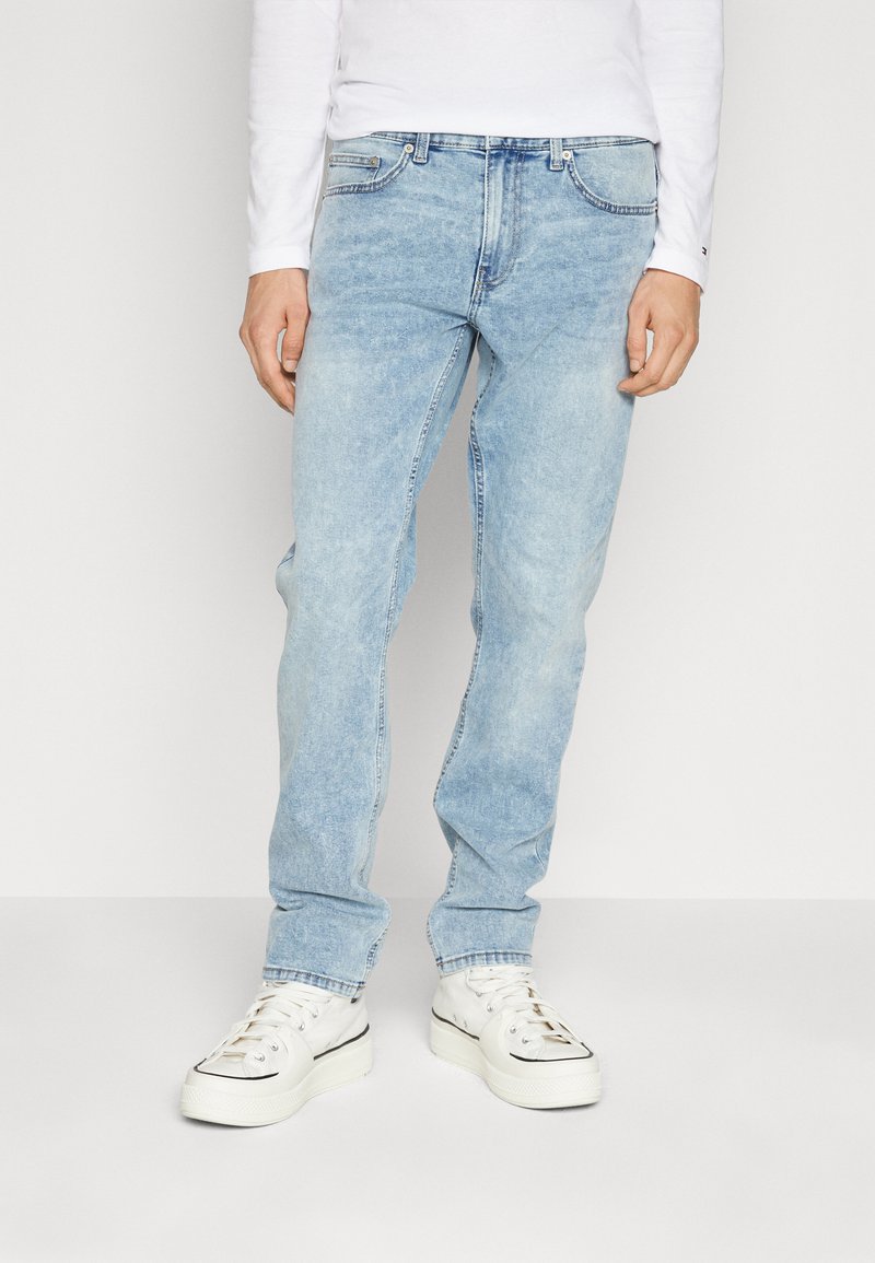 Ljusblå denimjeans med rak benpassform, femfickorsdesign och blekt utseende. Bärs med vita sneakers.