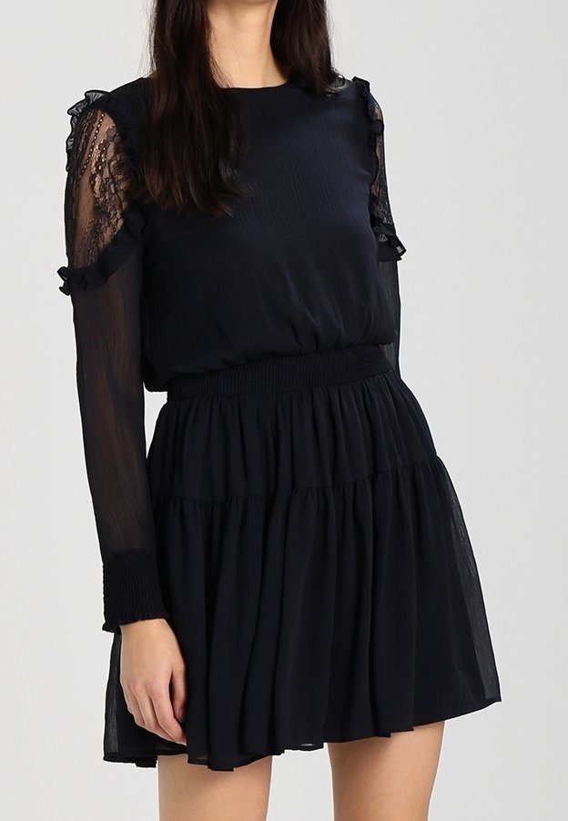 Černé šaty s texturovaným živůtkem a dlouhými průhlednými krajkovými rukávy. Obsahují nabíraný pás a vrstvenou sukni pro splývavý siluetu.