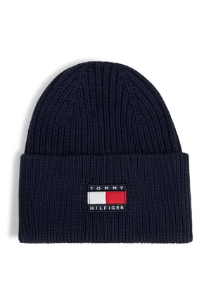 Navy blue knitted beanie with folded cuff featuring a rectangular Tommy Hilfiger logo patch in red, white, and navy colors.