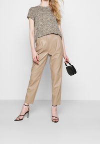 Haut à manches courtes avec un motif géométrique dans des tons terreux, associé à un pantalon taille haute en fausse cuir beige et des talons noirs à brides.