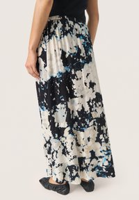 Maxirock in einem schwarz-weiß-blauen abstrakten Muster; plissierte Textur; elastischer Bund; kombiniert mit schwarzen, weichen Ballerinas.