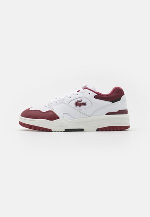 Lacoste Sneaker aus weißem Leder mit weinroten Akzenten, Netzdetails, einer klobigen Gummisohle und dem charakteristischen Logo an der Seite.