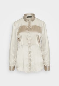 Blusa de seda cremosa con un cuello beige texturizado, con cierre de botones, mangas largas y paneles en contraste. Textura suave y brillante.