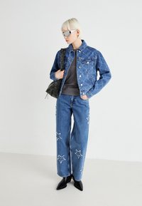 Denimjakke med quiltet mønster, kombinert med vide bukser med stjernesøm, svarte spisse sko og en mørk tote bag.