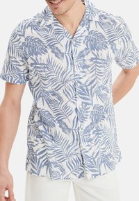 Camisa de manga corta de tela ligera, con un estampado de palmas azules en un fondo blanco. Botones destacados y un corte relajado.