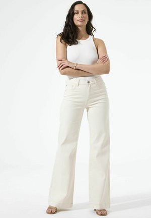 Witte tanktop en crèmekleurige jeans met wijde pijpen. De jeans hebben een hoge taille en een gladde textuur, met subtiele stiksels en voorzakken.