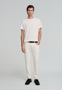Cremefarvet bomulds t-shirt med rund hals, parret med off-white bukser. Sort bælte og sorte sko fuldender looket.