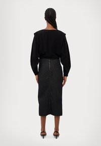 Svart blus med axelvaddar, kombinerad med en mörk denimpennkjol med dragkedja bak. Slät textur med skräddarsydd passform.