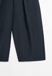 Mørkeblå vidbukser med synlige vandrette sømdetaljer nær kanten, vist mod en hvid baggrund.