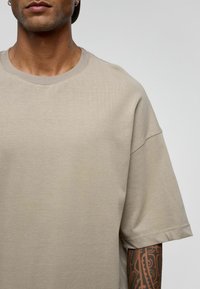 Beige t-shirt met korte mouwen, gemaakt van zachte, gladde stof, met een ronde halslijn en subtiele stiksels.