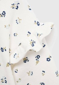 Biely textil s malými modrými a béžovými kvetinovými vzormi, s detailom volánového okraja.