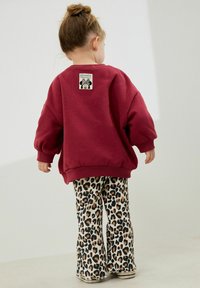 Burgunderfarbener Oversized-Sweatshirt mit Grafiklabel; kombiniert mit ausgestellt geschnittenen Leopardenmuster-Hosen, die eine Mischung aus Tiermustern und Texturen zeigen.