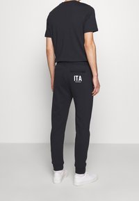 Men's black sportswear set, including a short-sleeve T-shirt and joggers. Joggers feature a back pocket with "ITA" and ribbed cuffs.