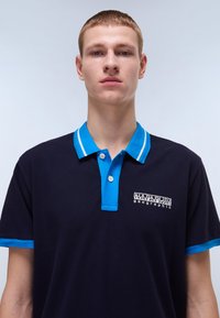 Marineblå polo med turkise detaljer på kragen og ermene, med to-knapps knappestang og brodert logo på brystet.