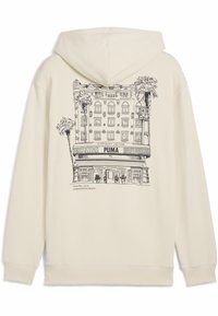 Felpa color crema con un'illustrazione in outline nera di un edificio con palme e il testo "PUMA" e "TUTTI SONO BENVENUTI."