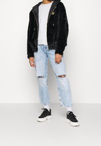 Sort faux fur zip-up hoodie med en grå crewneck t-shirt, slidte lyseblå jeans og sorte sneakers med hvide såler.