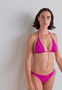 Rosa bikini med trekantet topp og sidesnøring, med et teksturert mønster. Materialet ser ut til å være elastisk, passende for badetøy.