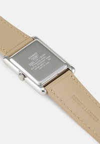 Casio rectangularni ručni sat s pozadinom od nehrđajućeg čelika, bež kožnim remenom od prave kože i graviranim detaljima. Vodootporan do 5 bara.