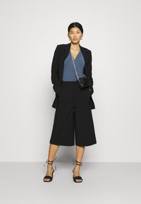 Pantaloni neri a vita alta e larghi, blazer aderente, top blu, sandali neri con tacco a strappo e una piccola borsa nera con tracolla a catena.