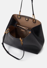 Czarna skórzana torba tote o gładkiej fakturze, z złotymi akcentami, wnętrzem z wzorzystą podszewką oraz zamykaną na zamek przegrodą.