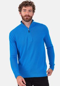 Pull léger bleu à fermeture éclair, manches longues, poignets et ourlet côtelés, en tissu doux. Présente un col à fermeture éclair quart de tour.