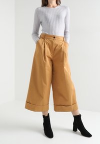 Grå ribbad långärmad topp i kombination med högmidjade, vida senapsgula byxor med uppvikta fållar och svarta snörstövletter.