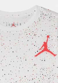 Biała koszula w czerwone i czarne kropki, z czerwonym logo Jumpman i napisem "JORDAN" blisko kołnierzyka.