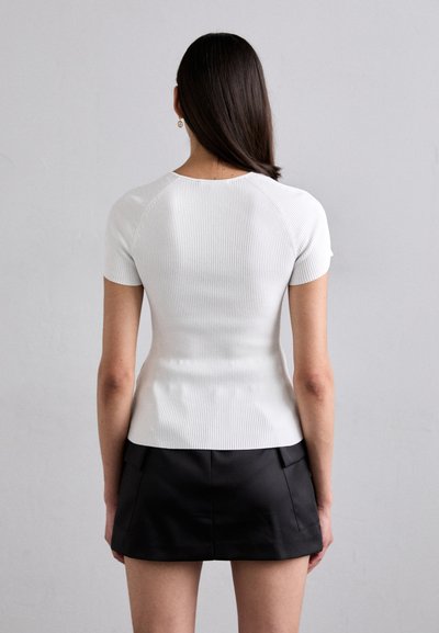 Witte geribbelde gebreide top met korte mouwen, getailleerd ontwerp, ronde halslijn, gecombineerd met een zwarte minirok, gladde textuur en schone lijnen.