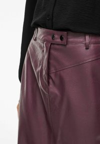 Bordeauxfarbene Lederrock mit glatter Textur, hoher Taille und zwei schwarzen Knöpfen an der Taille. Mit diagonalen Nähdetails.