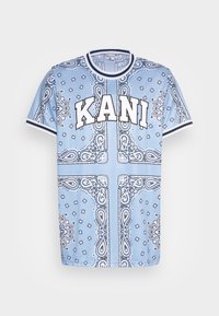 Lyseblå kortermet t-skjorte med bandana-mønster i svart og hvitt, med "KANI" trykt fremtredende på forsiden.