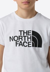 Biała bawełniana koszulka z dużym czarnym nadrukiem logo "The North Face" z zaokrąglonymi akcentami, krótkimi rękawami i klasycznym okrągłym dekoltem.
