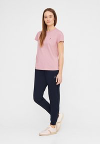 Helles pinkes Baumwoll-T-Shirt mit kurzen Ärmeln, kombiniert mit marineblauen Jogginghosen. Beigefarbene Sneakers mit hellen Akzenten runden das Outfit ab.