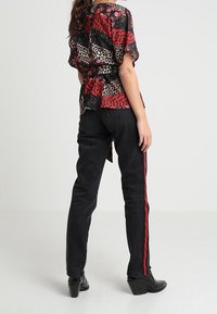 Rød og sort mønstret bluse med en knyttet detalje bagpå, parret med sorte jeans med røde sidelister og sorte hæl-sko.