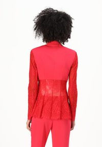 Rode blazer met lange kanten mouwen, met een gestructureerde lijfje en peplumontwerp. De kant heeft een ingewikkeld bloemenpatroon.
