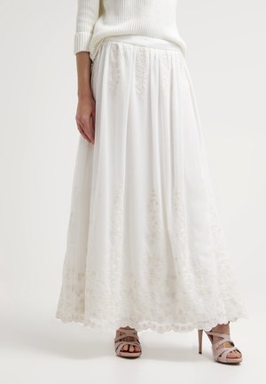 White embroidered maxi skirt worn with a white sweater and beige high-heeled sandals on a plain background.