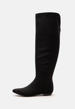 Botte haute plate en daim noir avec bout pointu et petit talon, vue de côté sur fond blanc.