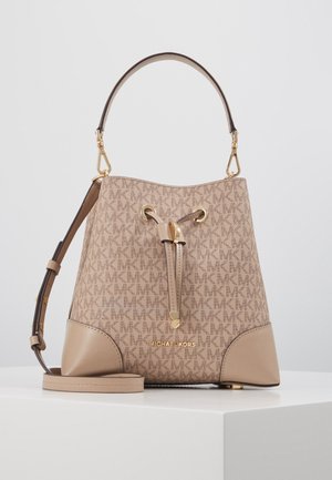 Sac seau beige Michael Kors avec motif logo MK, garnitures dorées, poignée supérieure et bandoulière ajustable sur surface blanche.