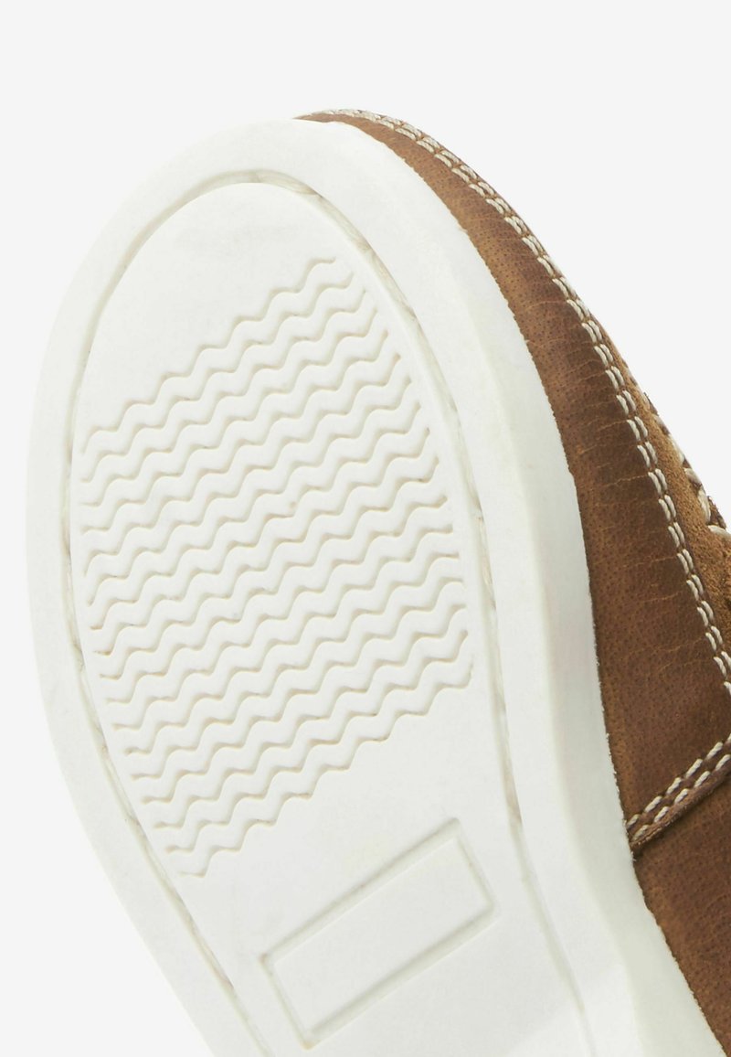 Chaussure en cuir marron avec une semelle en caoutchouc blanc présentant une texture ondulée. Les détails de couture le long du bord supérieur apportent un contraste.