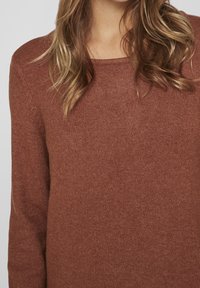 Maglione marrone lavorato a maglia con scollatura rotonda e maniche lunghe, caratterizzato da una trama morbida e una minimale decorazione.