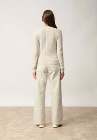 Beżowy sweter robiony na drutach z ribbowanym dołem, zestawiony z kremowymi szerokimi spodniami. Miękka faktura, dopasowane rękawy i prosty design.