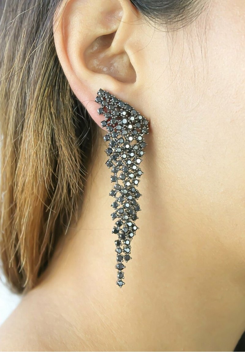 Longue boucle d’oreille en filigrane argenté avec des pierres précieuses noires et blanches portée à l’oreille gauche sur un fond de peau claire et de cheveux bruns.