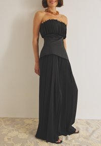 Juoda be petnešų palaidinė su klostuota tekstūra ir sluoksniuotu apvadu, derinama su plačiomis juodomis kelnėmis. Paprastas, elegantiškas dizainas su lygiu paviršiumi.