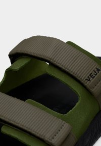 Sandale verte et kaki avec larges brides en textile, semelle intérieure texturée et semelle extérieure en caoutchouc noir durable. Le design comprend des accents découpés.