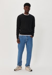 Black long-sleeve knit top layered over a white shirt, paired with light blue loose-fit jeans and beige sneakers with gray accents.